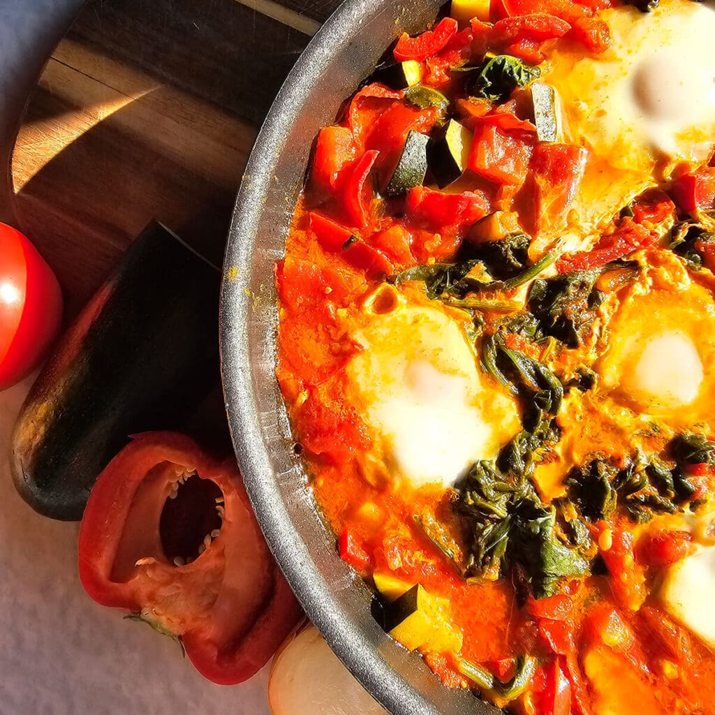 Pyszna jajecznica z warzywami i przyprawami w żeliwnym naczyniu, podana z pomidorami i czerwonymi paprykami na drewnianym stole.