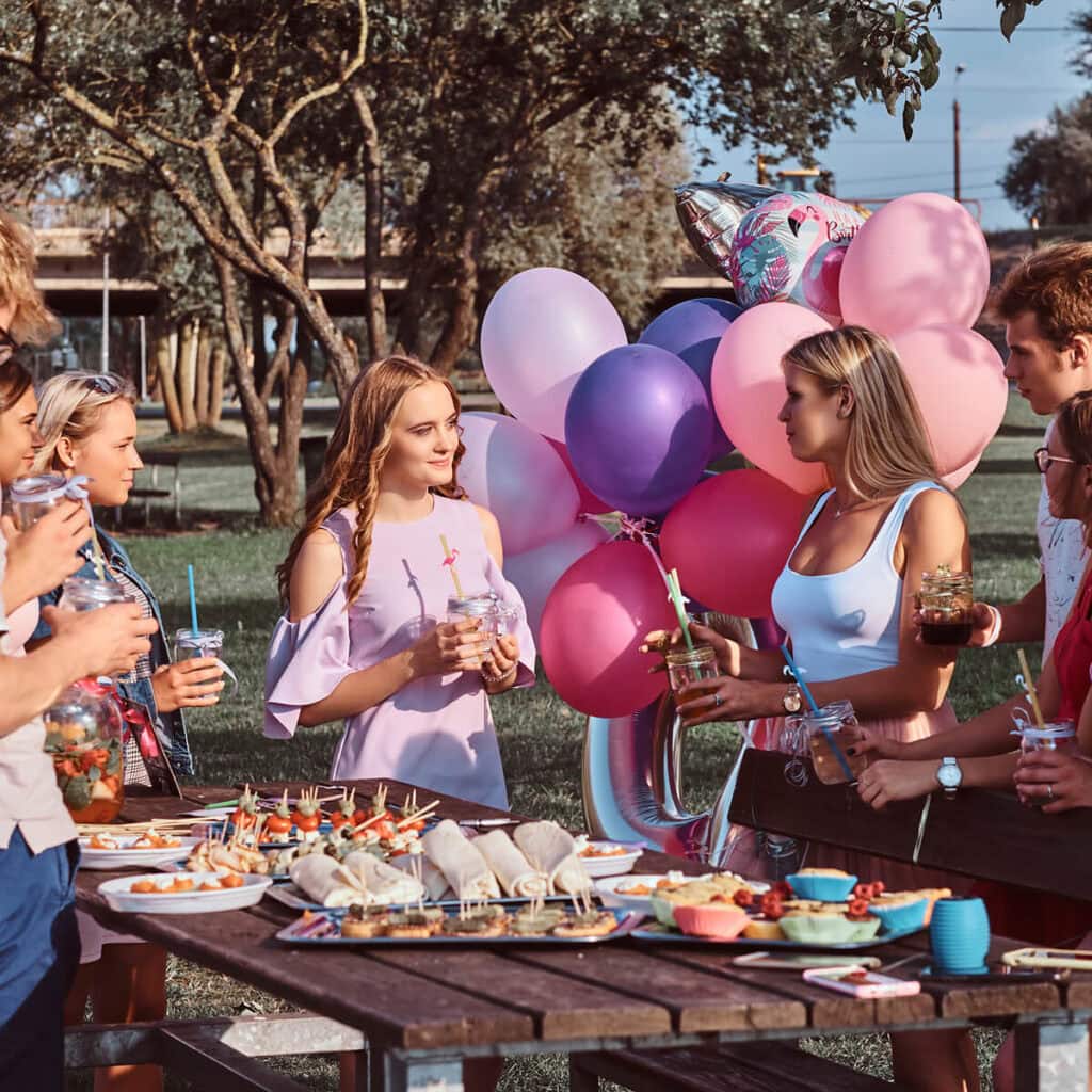 Kolorowe balony i impreza plenerowa z grupą młodych ludzi podczas pikniku lub urodzin na świeżym powietrzu.