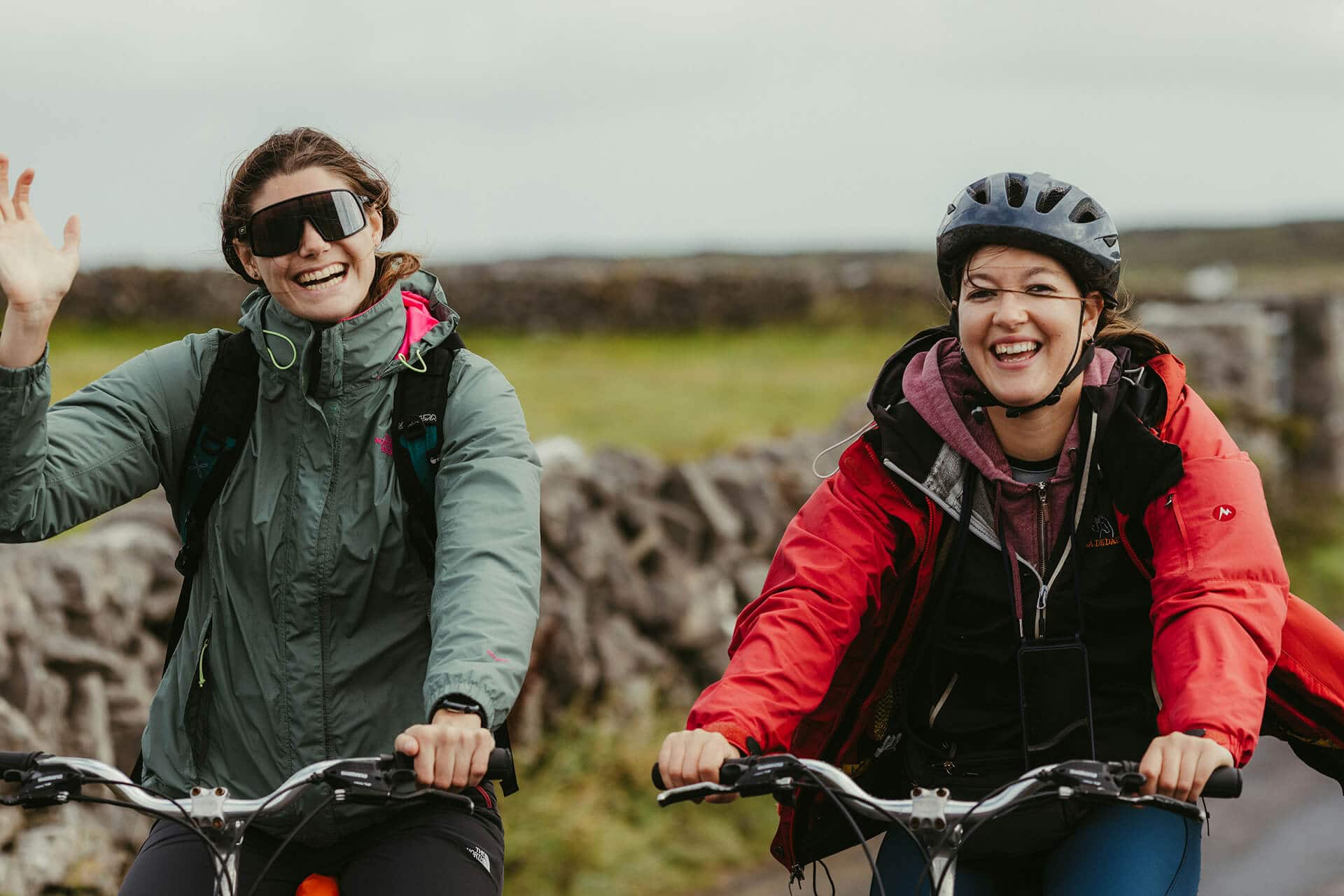 śmiejące się kobiety na rowerach, przyrodnicza sceneria, jazda na rowerze, przyjazna atmosfera, aktywny wypoczynek na łonie natury, outdoor, sport na świeżym powietrzu.