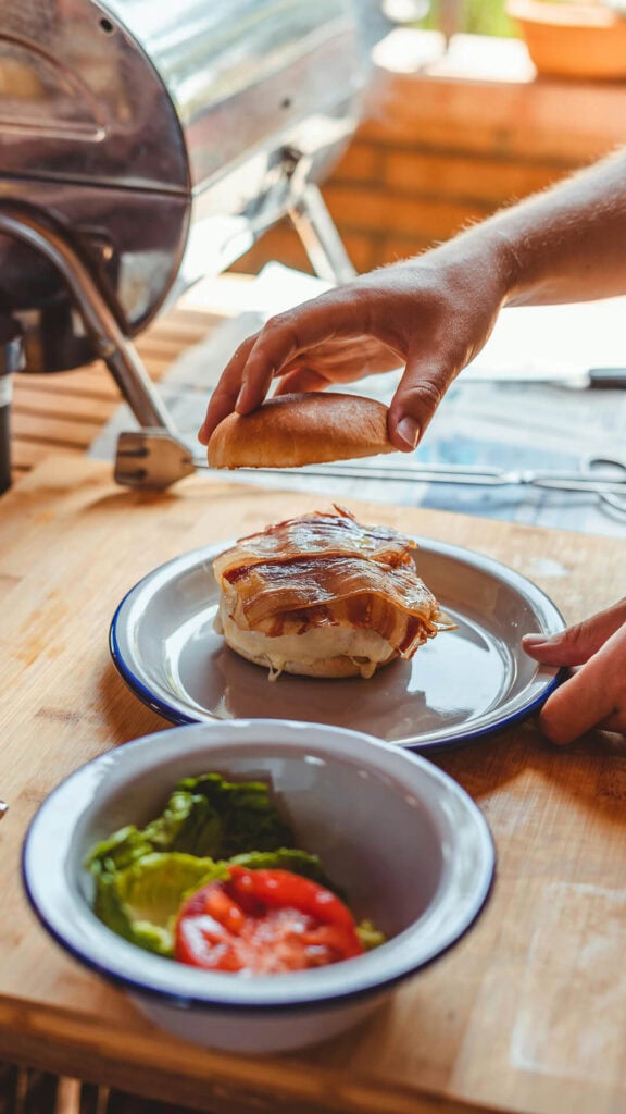 Stek Burger z boczkiem i warzywami na drewnianym stole, relaks w plenerze przy barbecue, ostre światło, gorąca atmosfera, menu restauracji relaxwterenie.pl.