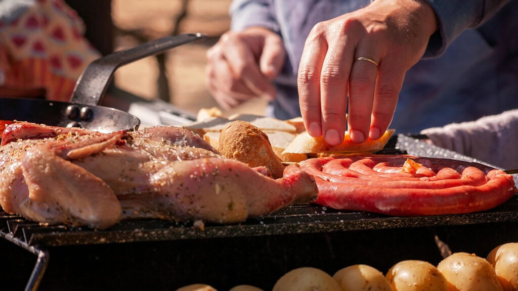 Widoczna ręka mężczyzny, który przygotowuje mięso na grillu.