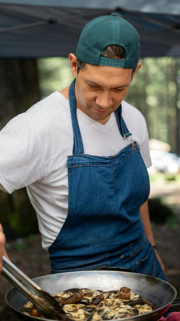 Pieczenie pizzy na świeżym powietrzu w parku, kucharz w czapce i fartuchu, cieszący się gotowaniem na zewnątrz.